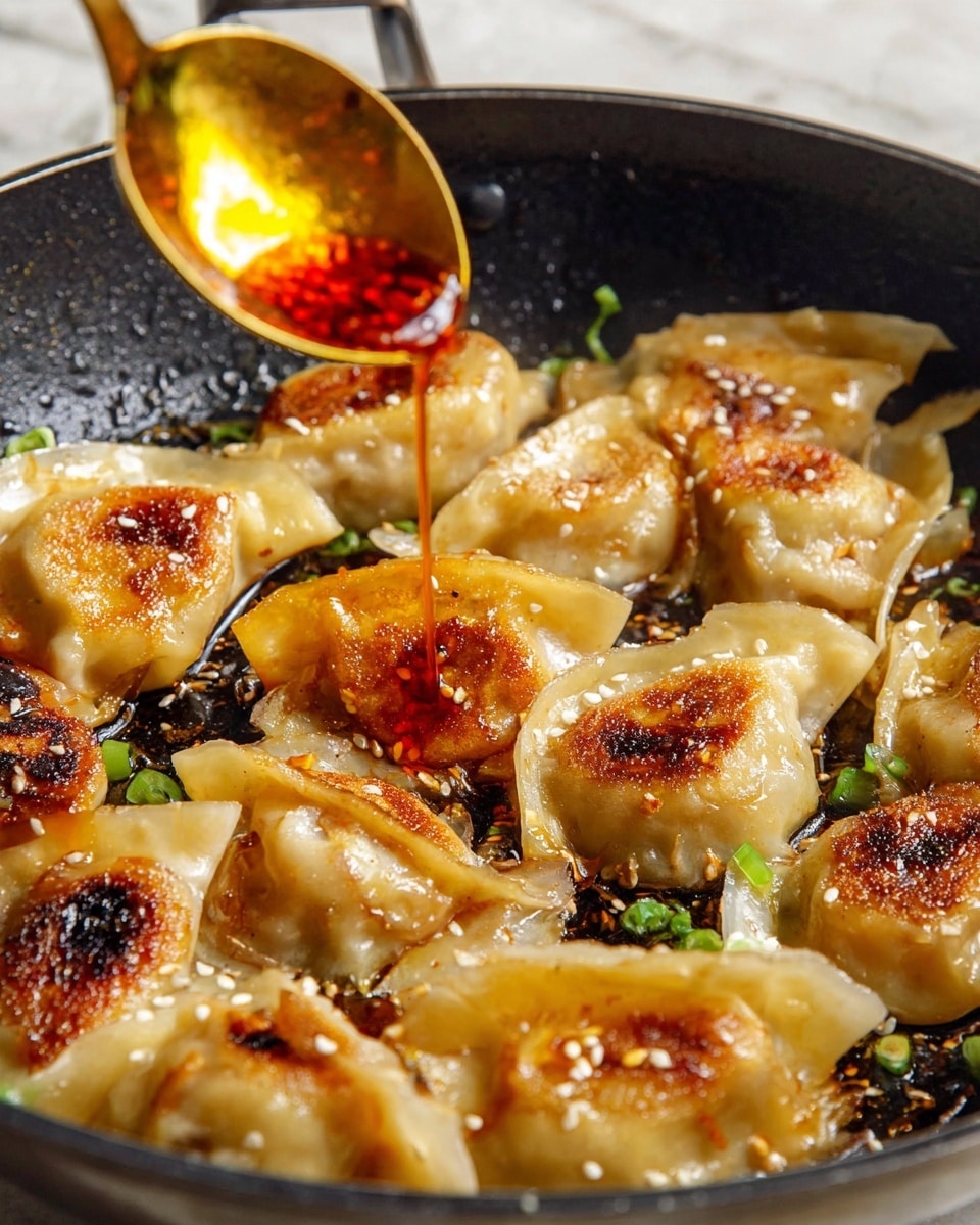 A close-up view of a frying pan filled with a single layer of golden-brown dumplings that have slightly crispy edges and soft, translucent dough. The dumplings are arranged closely, some showing light charring and sesame seeds on top, along with small bits of green onions scattered around. Above the pan, a gold spoon held by a woman's hand drips a bright orange-red chili oil sauce, adding a shiny layer on the dumplings. The pan's dark surface contrasts with the warm colors of the dumplings and sauce, all set on a white marbled texture. photo taken with an iphone --ar 4:5 --v 7