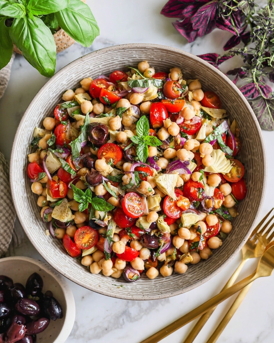 A bowl filled with a chickpea salad showing three main layers: the base layer of beige chickpeas, a mix of bright red halved cherry tomatoes and pale yellow artichoke pieces scattered through, and fresh green and purple basil leaves and mint on top, adding a leafy texture. The salad is served in a light grey textured bowl placed on a white marbled surface. To the right, partially visible gold cutlery rests beside the bowl, with a sprig of dark purple basil near the top corner. A cut red onion and black olives in a white bowl are seen near the bottom left. Photo taken with an iphone --ar 4:5 --v 7