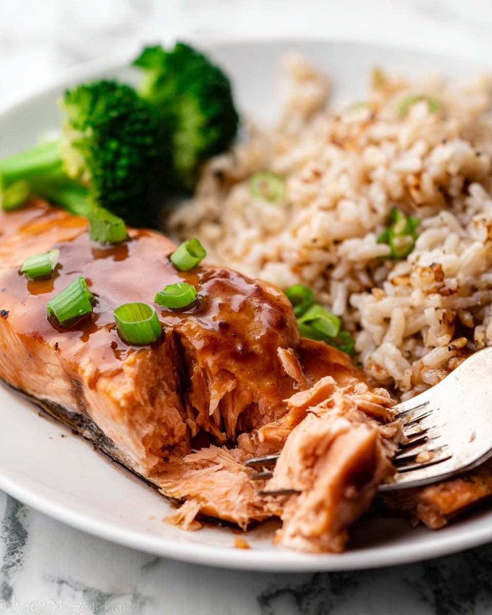 A white plate holds a meal with three main parts: on the left, a large piece of salmon cooked with a shiny brown sauce, topped with small green onion slices for decoration. The salmon is split into about two layers, showing its soft, pink inside. Behind the salmon, on the top left, two small green broccoli pieces add fresh color. On the right side of the plate, there's a pile of light brown rice mixed with darker bits, giving it texture. The rice forms a single layer that touches the salmon. The plate sits on a white marbled surface, and in the front right corner, a fork is lifting part of the salmon, showing more detail of its flaked texture. photo taken with an iphone --ar 4:5 --v 7