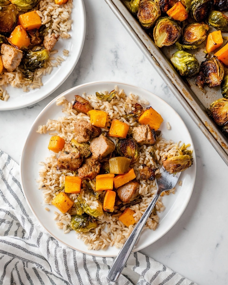 The image shows a white plate filled with a two-layer meal on a white marbled surface. The bottom layer is a bed of mixed wild and white rice with a soft and grainy texture. On top, there is a layer of roasted vegetables and meat pieces, including golden-orange cubes of roasted butternut squash, browned green Brussels sprouts halves, and small chunks of browned cooked meat with a slightly crispy outside. A silver fork lies on the right side of the plate, holding a piece of meat. In the background, parts of another white plate with the same meal and a metal baking tray with more roasted pieces are visible, alongside a striped cloth. Photo taken with an iphone --ar 4:5 --v 7