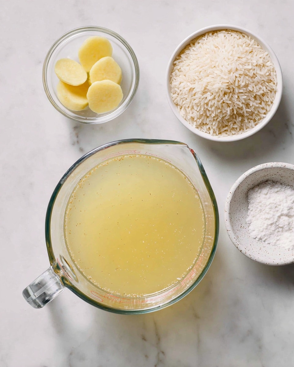 A clear glass measuring cup filled almost to the top with pale yellow broth, showing small specks inside, placed on a white marbled surface. To the right and slightly above the cup, there is a small clear bowl containing several smooth, rounded, light yellow slices. Below that, another clear bowl filled with white uncooked rice grains is present. At the far right, near the rice bowl, there is a small white speckled dish holding a small pile of white powder. All items are spaced out neatly on the white marbled surface photo taken with an iphone --ar 4:5 --v 7